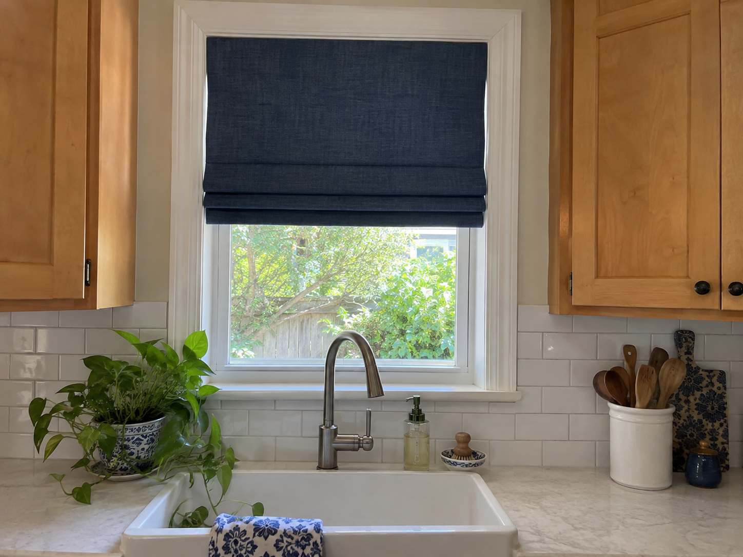 Illustration of a navy Roman shade with broad fabric folds above a kitchen sink